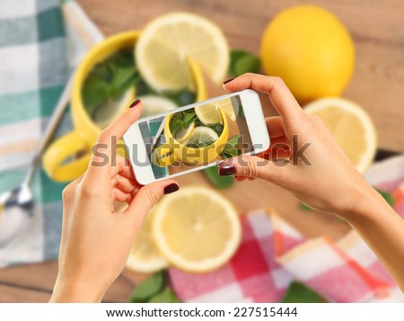 Woman taking photo of tea with lemon with smartphone