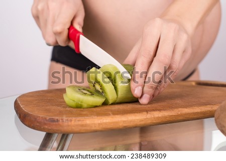 Portrait of pregnant mother cuts kiwi fruit on chopping board
