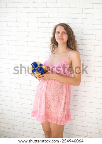 Pregnant woman with gift, against a white brick wall