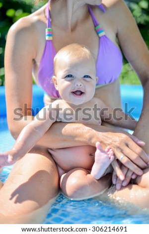 beautiful young brunette woman with her 6 months old baby relaxing in the swimming pool