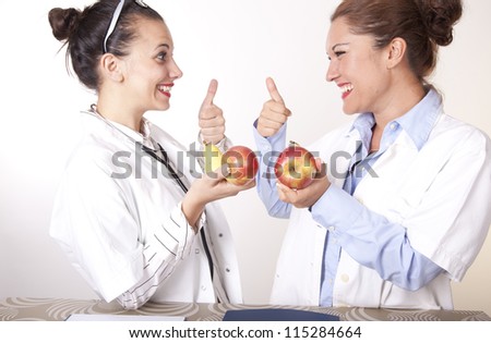 Portrait of a two young beautiful female doctors with apple showing thumb up.