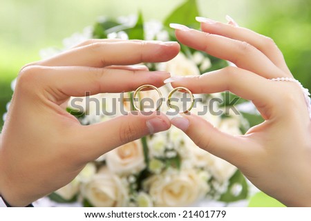 Bride and groom holding two rings over wedding bouquet