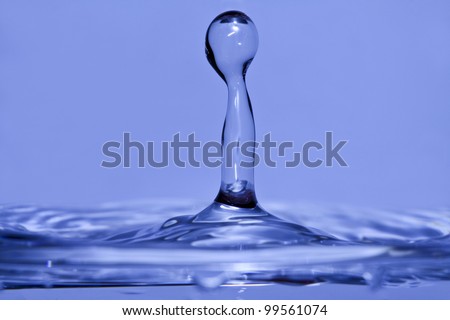Pure water drops splahing up. Blue reflections and ripples. One single tower of water./splashing water drop
