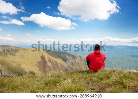 The young man sits on top of the mountain, in front of it is a beautiful landscape