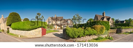 Welcoming family homes with well manicured hedges, gardens and pretty drystone walls, clear blue sky and warm early morning sunlight. Stitched panoramic image.