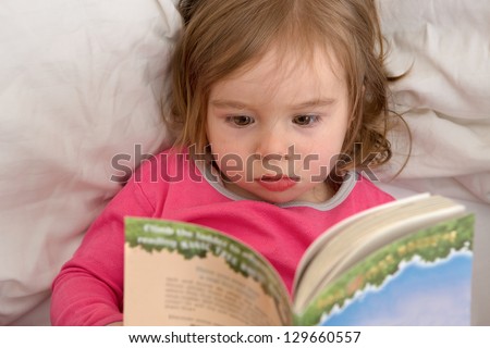 Cute toddler reading her stories before she goes to sleep. Reading habits starts with early age.