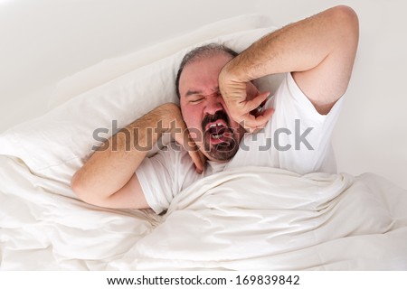 Tired man lying in bed stretching and yawning in an effort to wake up as he debates just turning over and going back to sleep in the morning