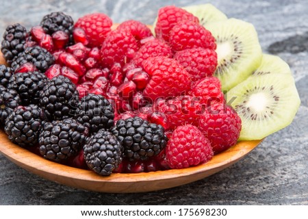 Bowl of fresh exotic tropical fruit with colorful neat rows of blackberries, pomegranate seeds, raspberries and thinly sliced kiwifruit on a stone counter for a delicious healthy vegetarian dessert