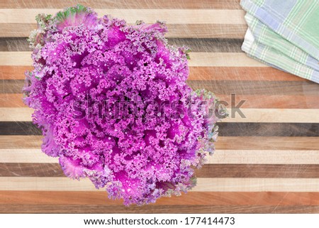 Ornamental curly-leaf purple kale, a healthy vegetable and cooking ingredient, on a decorative striped wooden board featuring different varieties of wood , view from above with copy space