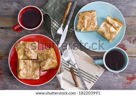 Tea for two at a spring picnic with cups of steaming hot tea and side plates with slices of freshly baked homemade borek pastry with napkins and cutlery on a rustic wooden table viewed from above