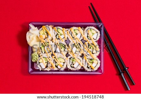 Punnet of sushi rolls to go with seaweed in plastic takeaway box, raw fish and rice served with traditional Japanese ninja chopsticks, overhead view on red