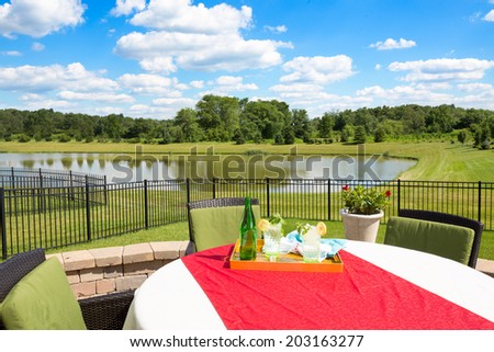 Glasses of fresh iced water garnished with fresh mint and lemon on a garden table covered in a colorful red cloth overlooking a tranquil pond and lush green countryside