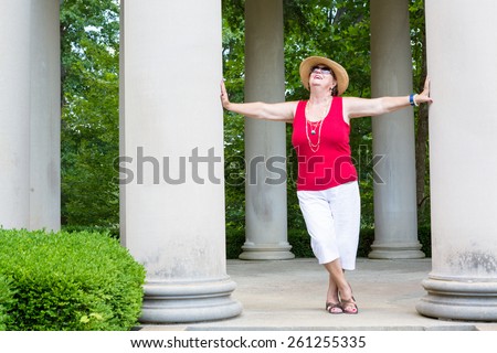 Happy Feel Good trendy modern grandma leaning with outstretched arms between two columns celebrating the sunshine and nature with her head tilted to the sun