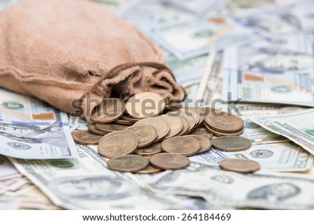 Golden dollar coins spilling from a hessian bag onto a background of US dollar bills with focus to the coins conceptual of wealth, winnings, growth returns, success, graft or money laundering concept