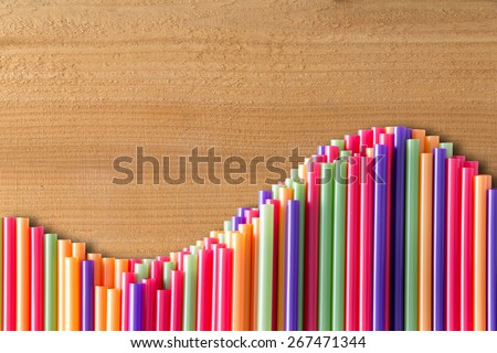What goes up must come down concept on wood with a wavy line of vivid multicolored drinking straws in an undulating pattern, with copy space