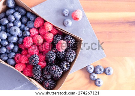 Box of fresh seasonal autumn berries with blueberries, blackberries, and raspberries displayed in a punnet on a wooden table fresh from the farmers market, with copy space