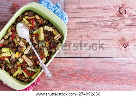 Baking dish filled with healthy roasted fresh vegetables for tasty vegetarian or vegan cuisine served on a rustic wooden table with copy space, overhead view