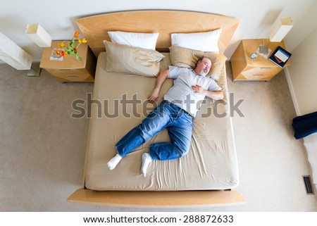 Overhead view of a big overweight middle-aged man with a goatee lying sprawled diagonally in his socks on a king size bed taking a midday nap over the weekend