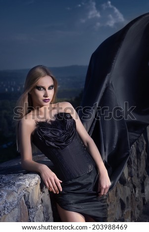 beautiful girl in a corset and dress with a long train at the stone wall. night sky background.