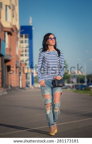 beautiful brunette girl walks through the city streets. in torn jeans and frock
