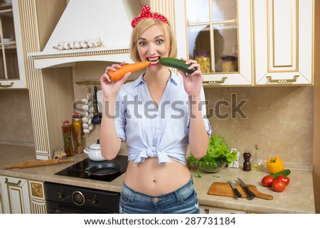 girl holding a big carrot and cucumber in the kitchen