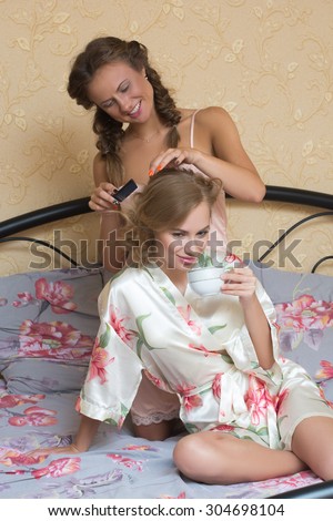 girl friends blond attractive young women sitting in bed in pajamas one doing other braid pigtail