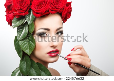 Beautiful woman with roses and leafs in her hair. She gets lipstick in preparation for her photo shooting.