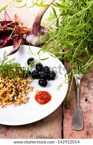 Buckwheat, pepper, black olives and herbs in white dish on  vintage dark wood background.
