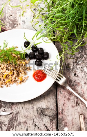 Russian cuisine. Buckwheat porridge, black olives and herbs on white plate on  vintage dark  background