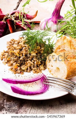 Russian cuisine. Buckwheat porridge, bresd, red onion  and herbs on white plate on rustic dark wooden table.
