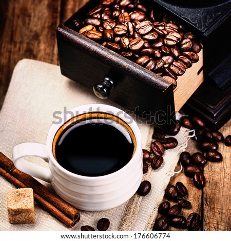 Cup of coffee with coffee beans and Coffee grinder on wooden brown background closeup.  Espresso Cup on brown napkin with cinnamon and sugar.