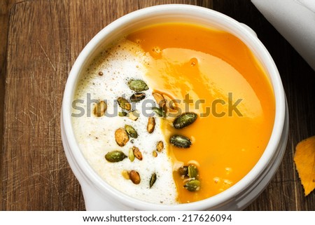 Pumpkin Soup with whipped cream and pumpkin seeds in a white plate over wooden background.  Beautiful autumn Pumpkin thanksgiving soup