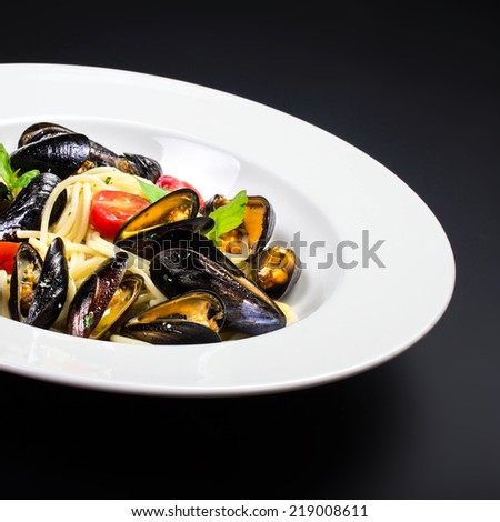 Pasta with mussels and basil for a tasty sea food meal over black table with copy space,  close up.
