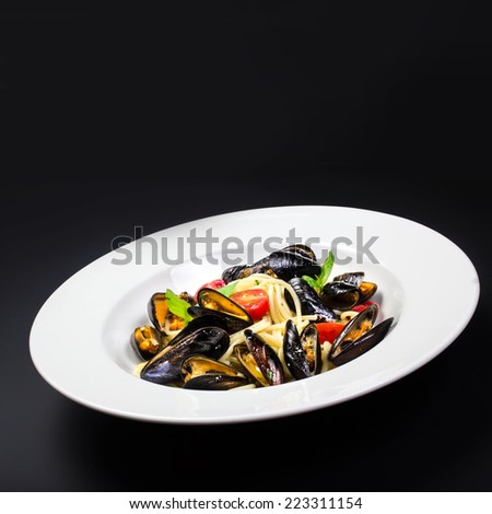 Italian pasta with Mussels marinara, cherry tomatoes and herbs for a tasty seafood meal over black table with copy space, close up