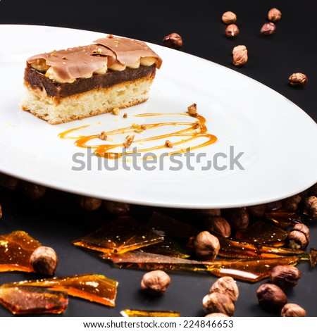 Chocolate Layer Cake with caramel, nuts and chocolate on white plate over black background, studio shot, close up. Italian sweet dessert concept.