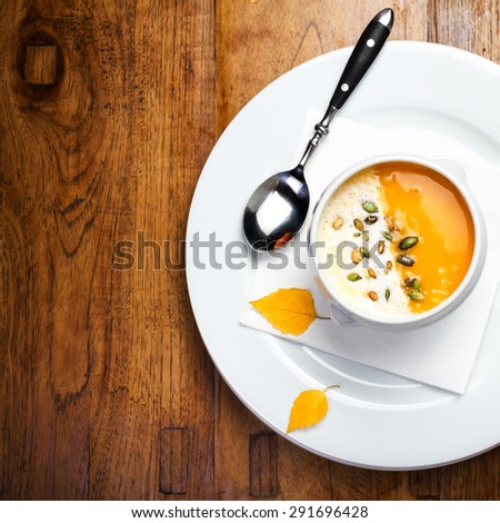 Pumpkin soup with cream and pumpkin seeds in a white bowl on wooden table