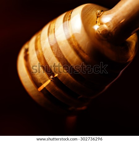 Wooden dipper with yellow honey flowing over dark chocolate colored swirl background macro. Golden Honey dip