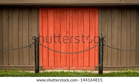 Single rustic red barn door flanked by brown wood planks and black metal posts with chains