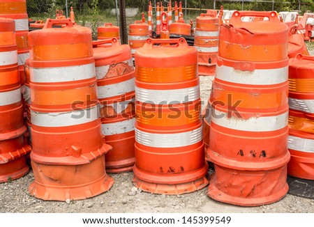 Multiple orange construction barrels stacked at a storage facility