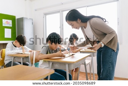 Portriat of  Asian female teacher helping elementary school boy in classroom at school. Education, elementary school, learning concept.