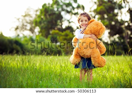 Little cute girl standing in the grass holding large teddy bear