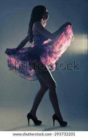 Silhouette of a beautiful tall woman dancing in purple dress in studio