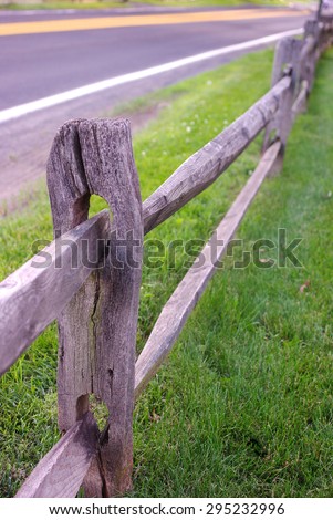Split rail fence at edge of grassy pasture meets up with blacktop road, both trailing off into the distance.