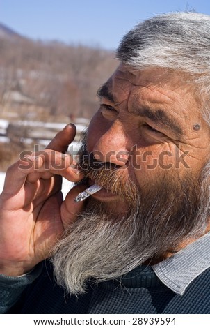 A portrait close up of the old smoking man with grey beard.