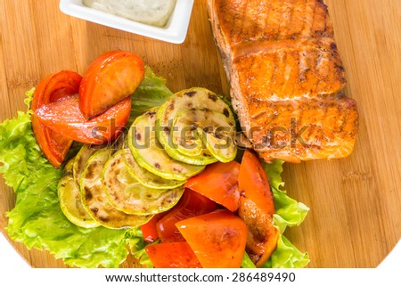 Tasty salmon steak with grilled vegetables, sauce and lemon on a wooden board