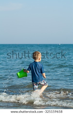 baby boy is playing with water on beach with beach toy, bucket. Summer time. Small waves. Wet sand. Bibione, Italy.