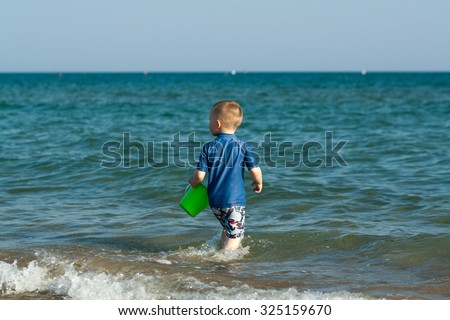 baby boy is playing with water on beach with beach toy, bucket. Summer time. Small waves. Wet sand. Bibione, Italy.