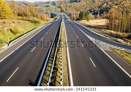 Empty highway between deciduous trees in autumn colors, in the distance electronic toll gates, view from above