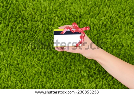 Woman hand holding a gift card with a red ribbon isolated on green background