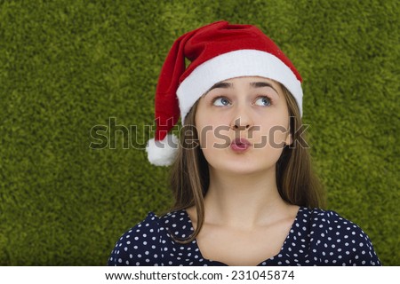 Confused young woman with a red santa claus hat looking up.Concept what to choose.Face emotion isolated on green background.